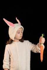 Foto de estudio de una niña con un disfraz de conejo de pascua y unas zanahorias. Fondo negro
