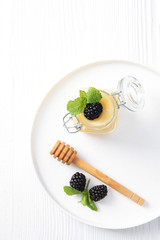 Yellow whipped honey on a white plate with a stirring stick and a BlackBerry berry. Photo on white background. Copy space.