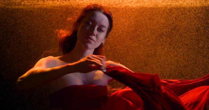 a cute girl with long hair moves her hands beautifully with a red cloth in a stream of bubbles under the water. contour bright orange light. close up