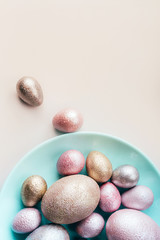 Colored painted pearl chicken and quail eggs of pink, silver, golden color on a blue mint plate pastel background. Minimalistic creative neo easter festive vertical flat lay. Copyspace for text