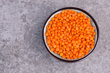 Red lentils in a bowl on a grey structured background