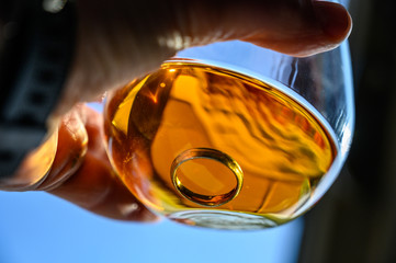 Caucasian hand holding a glass of amber colored liquid with a wedding ring at the bottom