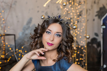 Fototapeta premium Beautiful brunette girl with a golden crown. Beauty face.Fashion Portrait of Beautiful Girl in exquisite jewelry. Beauty sexy Portrait. model with red lips in a crown and earrings is looking at the