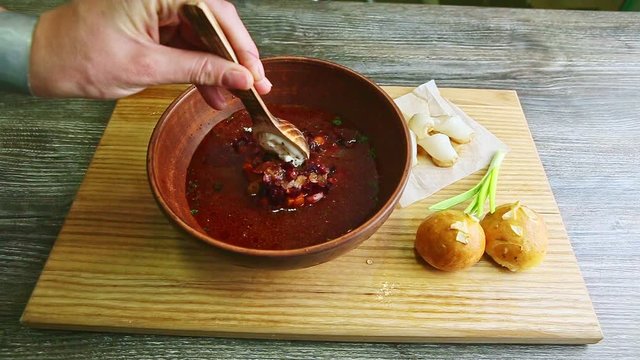 human hands mix traditional borscht and sour cream with wooden spoon