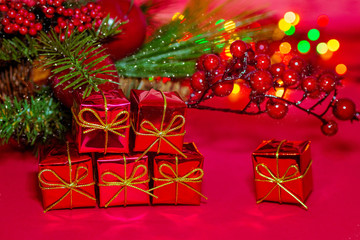 Christmas gift boxes on red background. Holiday card. Composition of fir branches, berries, Apple and bokeh lights garland. Gifts with gold ribbons and bows. The atmosphere of the new year.