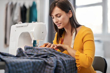 Focused charming caucasian fashion designer sitting in her studio and sewing beautiful dress.
