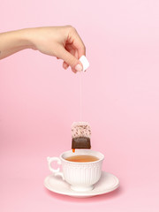 girl brews a tea bag in a white porcelain cup. Pink background