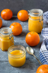 Tangerine jam in glass jars and fresh tangerines on a wooden table.