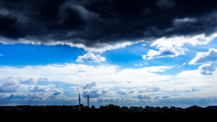The rays of the sun breaking through the dark evening clouds over a Muslim city. Silhouettes of two mosque minarets on the background of a bright dramatic sky. Allah sends its rays to the earth
