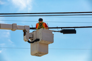 A low angled shot of a man at work in a mobile elevating work platform, MEWP or cherry picker, repairing and maintenance of overhead power cables
