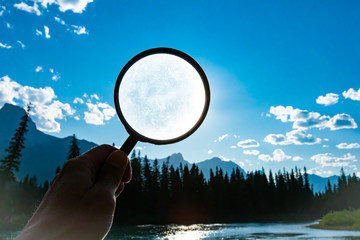  man holding a magnifying glass over a bright blue sky with scattered clouds during summer in nature with copy space