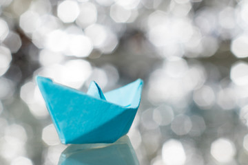 Blue paper ship, blurry lights on background, bokeh.