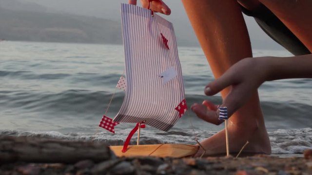 Girl plays with handmade toy sail ship with flags on the beach, sea waves, seascape.