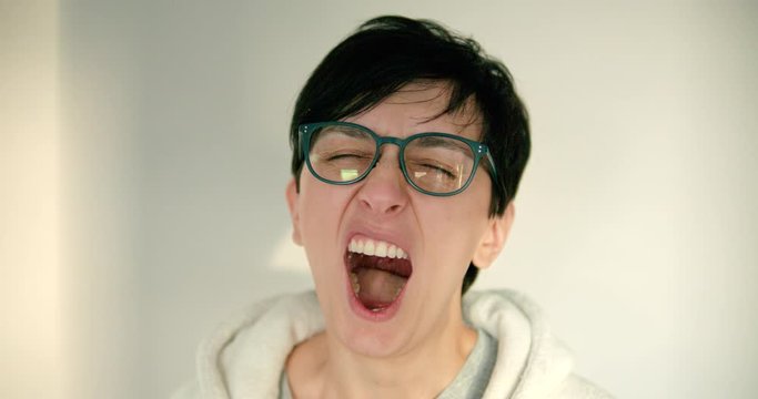 Close up of young woman with glasses and short hair yawning in slow motion
