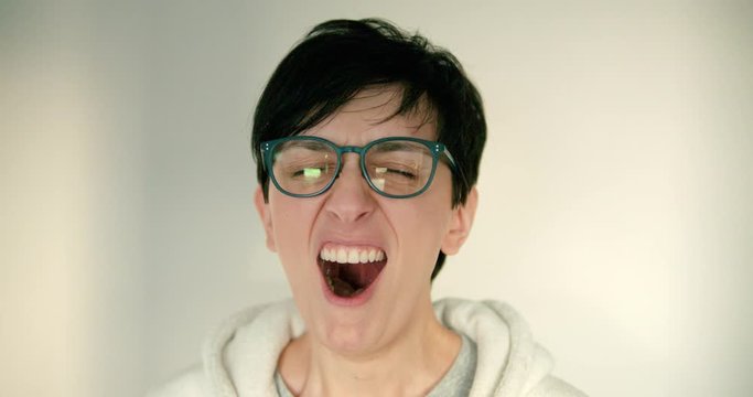 Close up of young woman and with glasses and short hair is tired and yawning