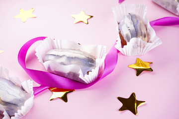 Eclairs with confetti in the form of stars and a purple ribbon on a pink background. French dessert.
