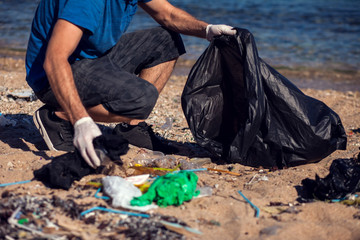 Man with black bag collect garbage on the beach. Environmental pollution concept