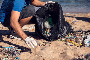 Man with black bag collect garbage on the beach. Environmental pollution concept