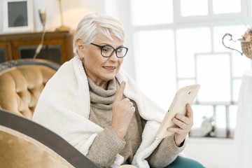 Elegant Senior Woman In Woolen Sweater Is Reading Something Pleasant On Her Tablet