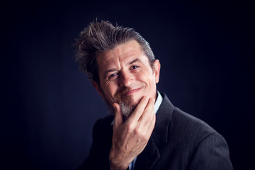 Half bearded man wearing suit scratching his face in front of black background. People and skin...