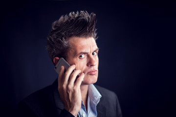 Man with mohawk wearing suit using mobile phone in front of black background.