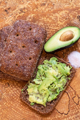 Avocado on a wooden background and bread, avocado spread on a piece of rye bread, pink salt.