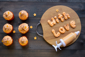 Cupcakes with orange cream icing on wooden board, top view or flat lay. Confectionery syringe...