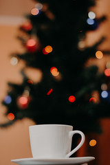 Obraz premium White color cup of coffee with Christmas tree in the background