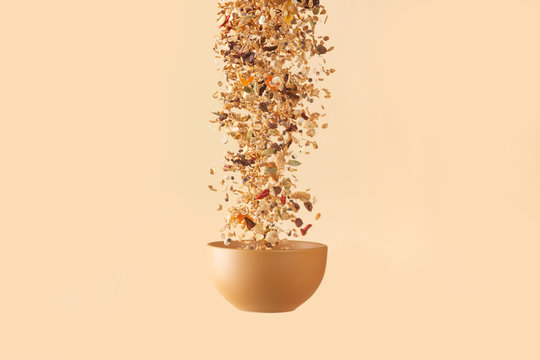 Falling granola with candied fruits and nuts  to baige flying bowl on baige background.