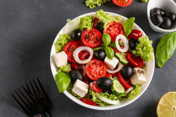 Healthy Greek salad of green lettuce, cherry tomato, onion, pepper, feta cheese, black olives, basil, cucumbers, with olive oil and lemon juice, Top view