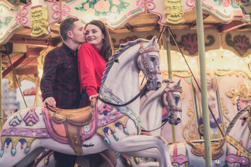 Obraz na płótnie Canvas romantic couple taking a moment to kiss while riding horses on carousel