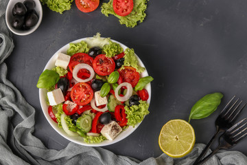 Healthy Greek salad of green lettuce, cherry tomato, onion, pepper, feta cheese, black olives, basil, cucumbers, with olive oil and lemon juice, Closeup, Top view