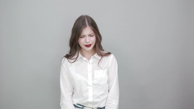 Boring young woman in fashion white shirt isolated on gray background in studio yawning, holding hand on head, sleepy. People sincere emotions, lifestyle concept.