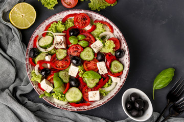 Healthy Greek salad of green lettuce, cherry tomato, onion, pepper, feta cheese, black olives, basil, cucumbers, with olive oil and lemon juice, Top view