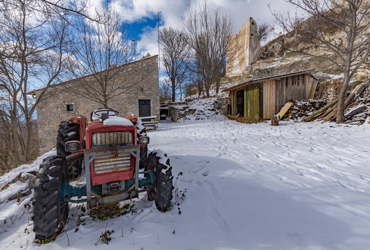 Rural mountain scene of an old tractor parked in a snowy courtyard