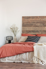 Cozy bedroom interior with white walls, wooden bedhead and red sheets. Real photo