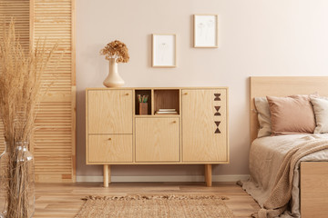 Flowers in vase on wooden commode in simple bedroom interior