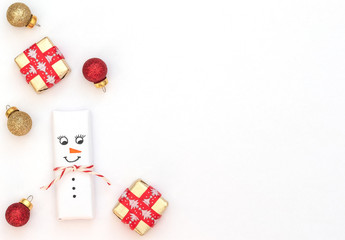 Christmas white background with snowman, wrapped gift box with red ribbon and red and gold Xmas balls. New Year greeting card. Christmas, New Year concept. Flat lay style with copy space.