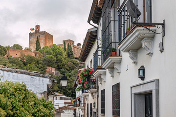 Fototapeta na wymiar Narrow street in Granada, Spain with view of the Alhambra in background. Narrow hilly street in Granada, Andalusia, Spain