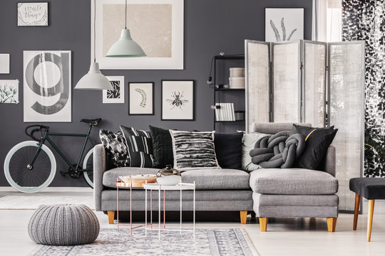 Stylish industrial coffee table with vase and plate next to grey scandinavian corner sofa with pillows in monochromatic interior