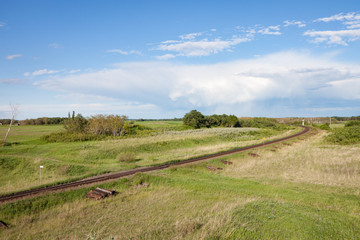 Railroad Track Curving Through Green Countryside Under Cloudy Blue Storm Sky