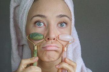 Woman making massage with green jade roller. Beauty tools for face treatment. Funny face.