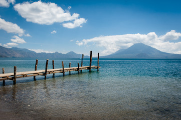 Pier stretches out through a clear lake with volcanoes in the background in Central America
