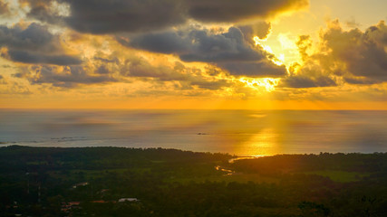 Spectacular sunset over the pacific while the sun's rays are breaking through the clouds over the ocean and the mainland. Amazing view over the jungle and the ocean with many tone colours on the sky.