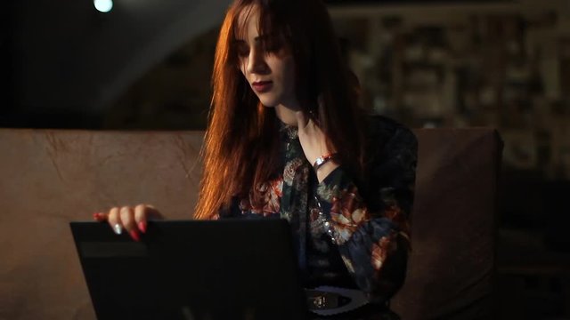 Uncomfortable position for using a laptop and neck pain. Red hair woman tired and exhausted, working late at night from home. Body discomfort and overworking concept