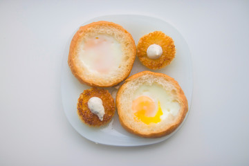 fried eggs baked in round bread with croutons on a white plate top view