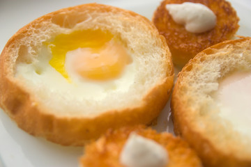 fried eggs baked in round bread with croutons on a white plate top view close up