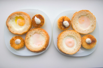 fried eggs baked in round bread with croutons on a white plate top view