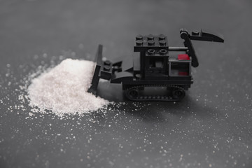 black toy bulldozer from designer blocks removes a mountain of salt on a black background