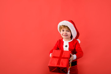 Santa helper holds box with present gift. Christmas children. Little kids celebrating Christmas. Child with Christmas present. Happy boy in Santa costume holds present. New year kid. Funny wintertime.